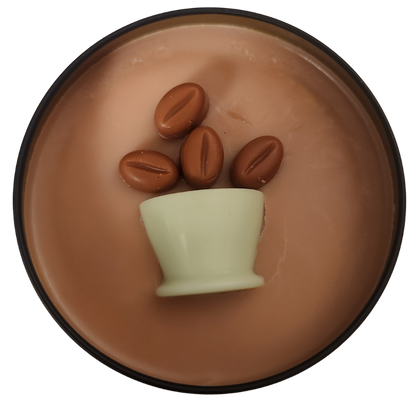 A black candle tin with tan wax and a green wax coffee mug with brown wax coffee beans coming out of the mug on a transparent background.