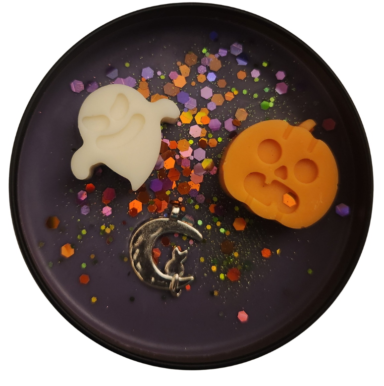A black candle tin with purple wax featuring an off-white ghost-shaped mold, an orange pumpkin-shaped mold, and a silver crescent moon with a cat silhouette, surrounded by colorful confetti.